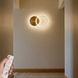 Aplique de pared LED decorativo de doble aro dorado en pasillo minimalista.