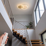 Lámpara de techo circular dorada iluminando zona de escaleras de diseño moderno.