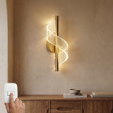 Aplique de pared Helix Gold con diseño helicoidal instalado verticalmente sobre un mueble de madera en una sala moderna.