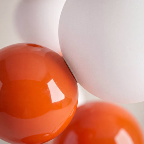 Detalle en primer plano de esferas cerámicas naranja y difusores de vidrio opalino de alta calidad.