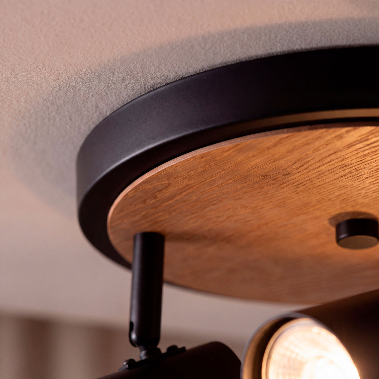 Detalle en primer plano del florón metálico en negro mate combinado con placa de madera natural.