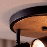 Detalle en primer plano del florón metálico en negro mate combinado con placa de madera natural.