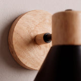 Detalle en primer plano de florón en madera natural y brazo metálico con pintura electrostática mate.