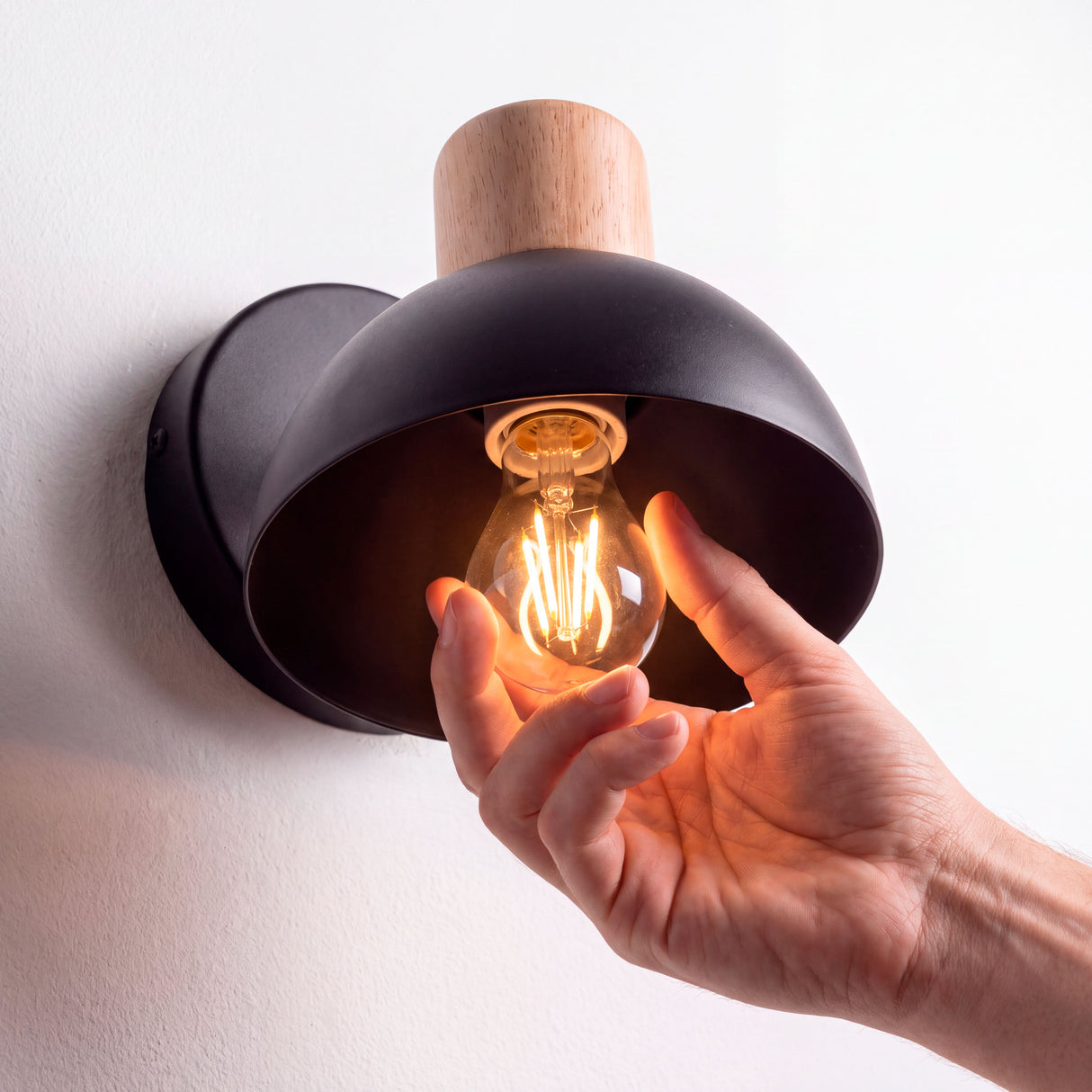 Mano instalando foco E27 en la campana del aplique, foco no incluido