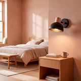 Aplique de pared negro iluminando velador de madera en dormitorio