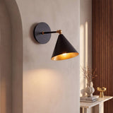 Aplique de pared BRERA negro y dorado encendido sobre muro limewash con panel de nogal