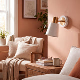 Aplique de pared blanco y dorado iluminando dormitorio en tonos durazno
