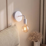 Aplique de pared blanco con foco vintage encendido junto a la cabecera