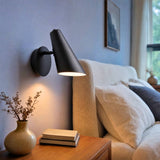 Aplique de pared LENA BLACK encendido junto a la cabecera de un dormitorio decorado