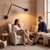 Aplique de pared negro iluminando rincón de lectura con pareja en casa