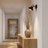 Aplique de pared negro iluminando pasillo con consola de madera