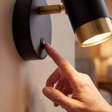 Mano encendiendo el aplique con su interruptor integrado en la base