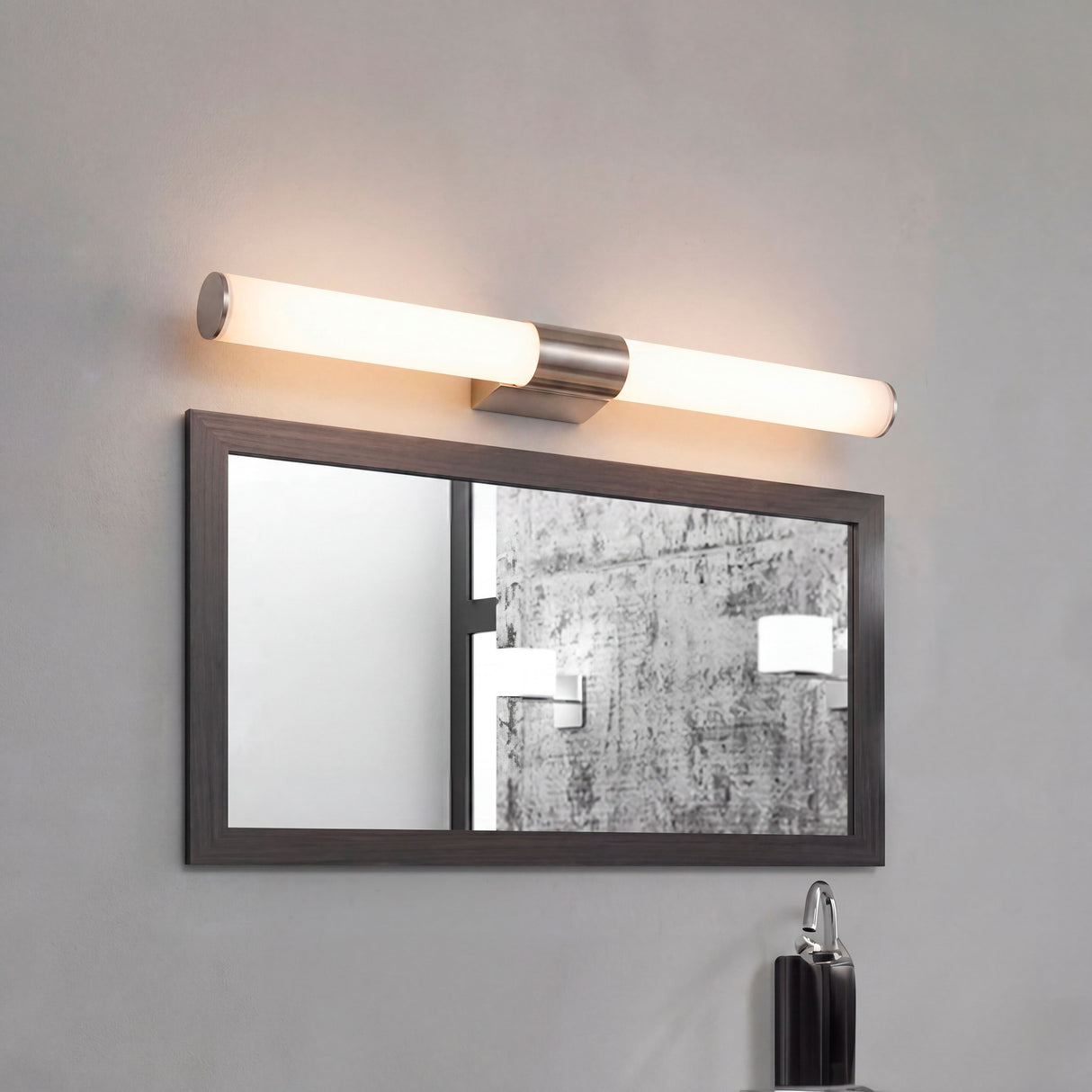 Lámpara de pared cilíndrica Nery Silver de 12W sobre espejo con marco negro.