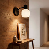 Aplique de pared con tulipa de cristal acanalado blanco y soporte negro para iluminación de acento en recibidor.