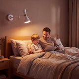 Padre e hijo leyendo en la cama bajo la luz cálida del aplique de velador blanco