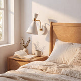 Aplique de velador blanco y dorado junto a cama de madera en dormitorio nórdico