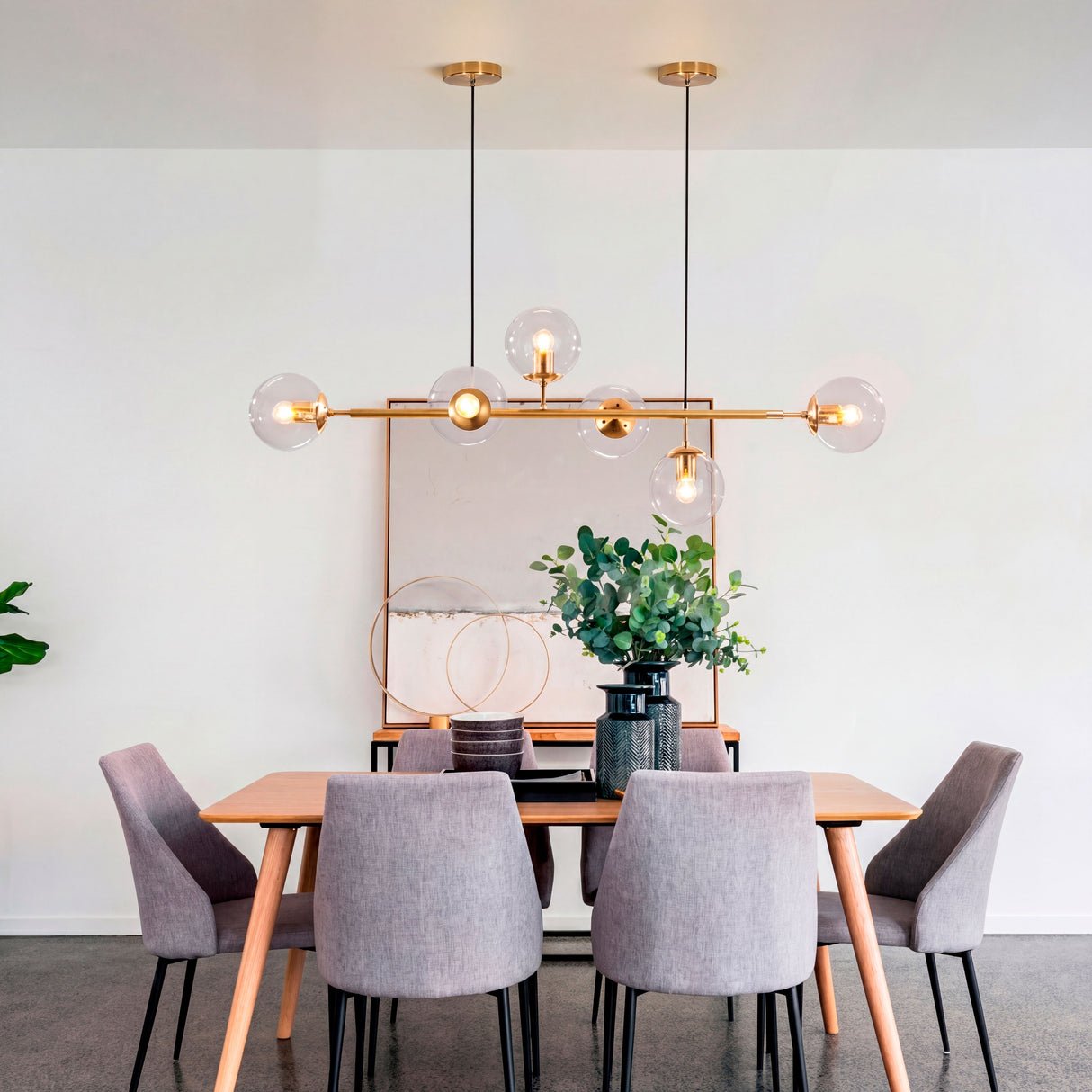 La lámpara Amber Line Gold centrada sobre una mesa de madera clara con sillas blancas.