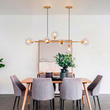 La lámpara Amber Line Gold centrada sobre una mesa de madera clara con sillas blancas.