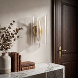 Detalle decorativo de lámpara de pared junto a florero en mesa de recibidor.