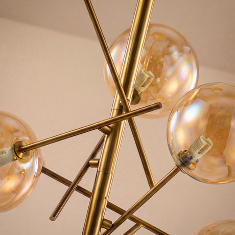 Primer plano de los brazos cruzados dorados y esferas de vidrio ambar de la lampara Estelar Gold.