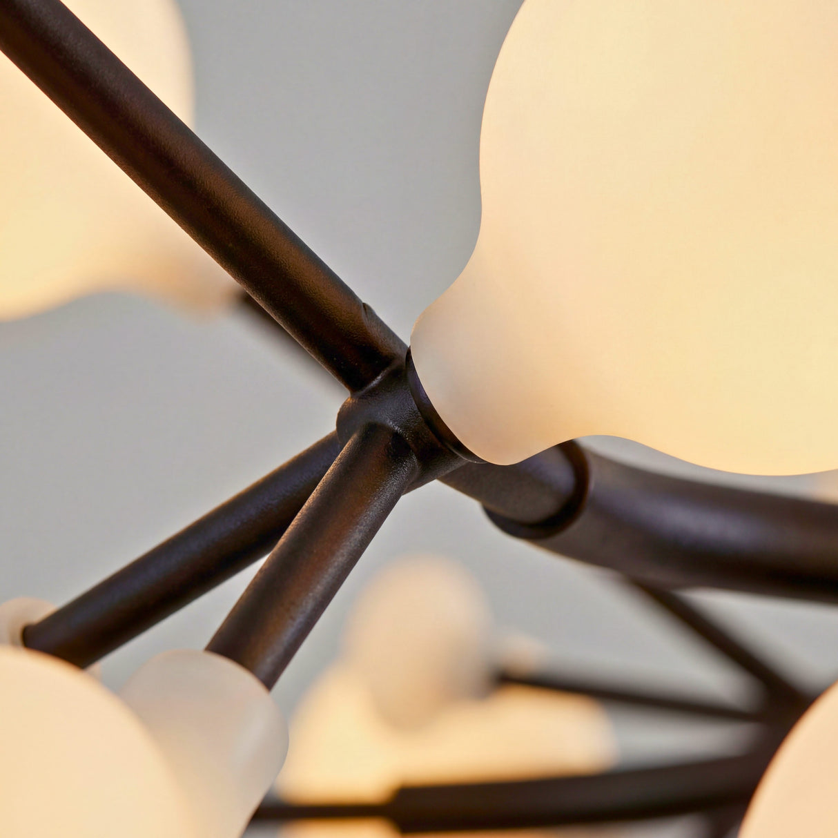 Primer plano de la union de los brazos negros y la esfera de vidrio opalino de la lampara Nativa.