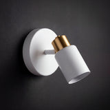 Foco direccionable blanco mate con detalle dorado destacando sobre muro negro con diseño minimalista.