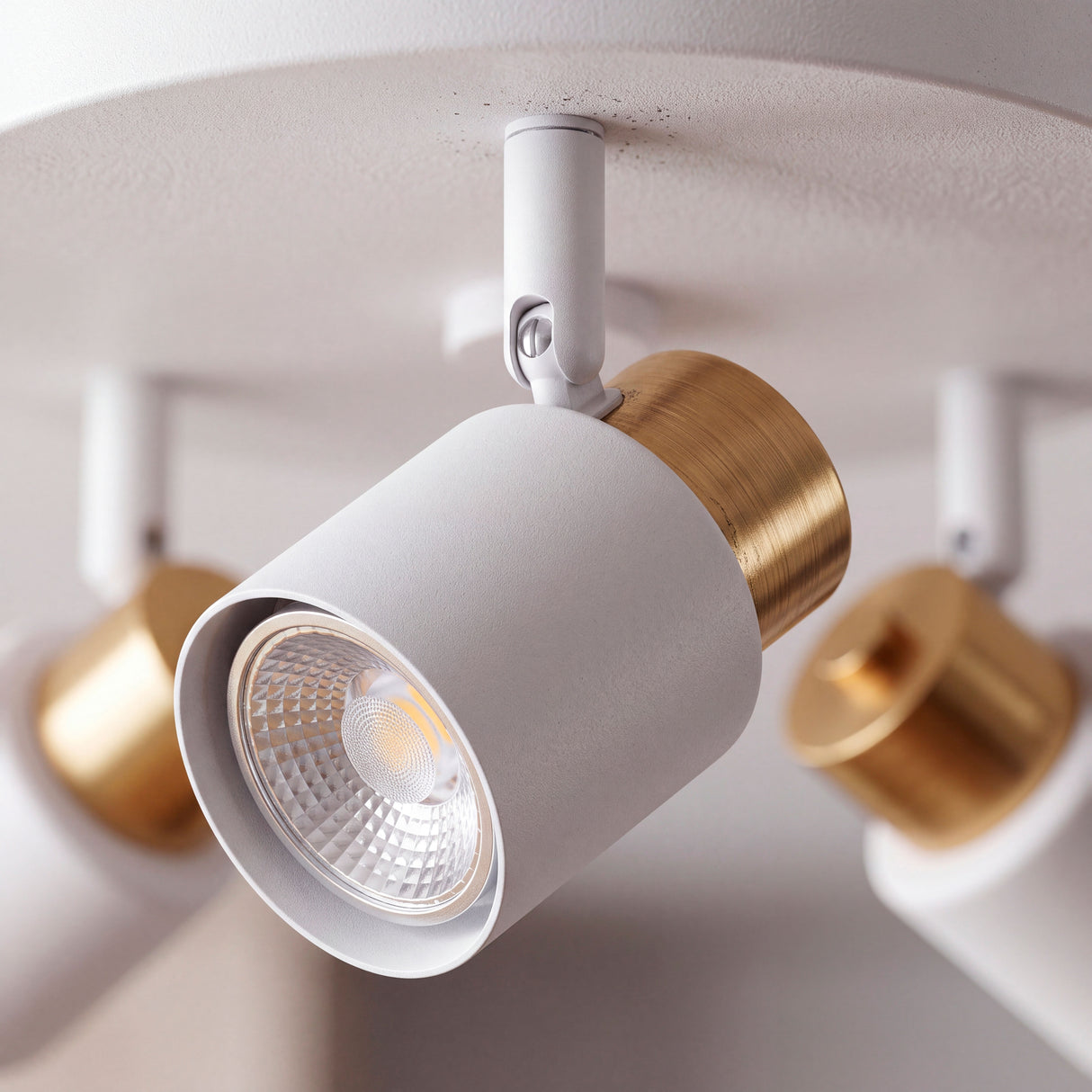 Primer plano de reflector cilíndrico en blanco mate con detalle de anillo dorado y rótula articulada.