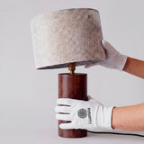 Proceso de instalación de pantalla beige sobre base cilíndrica oscura con guantes de microfibra.