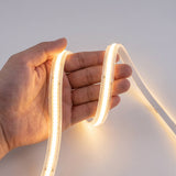 Mano sujetando tira luminosa flexible que muestra la distribución uniforme del flujo cromático cálido.