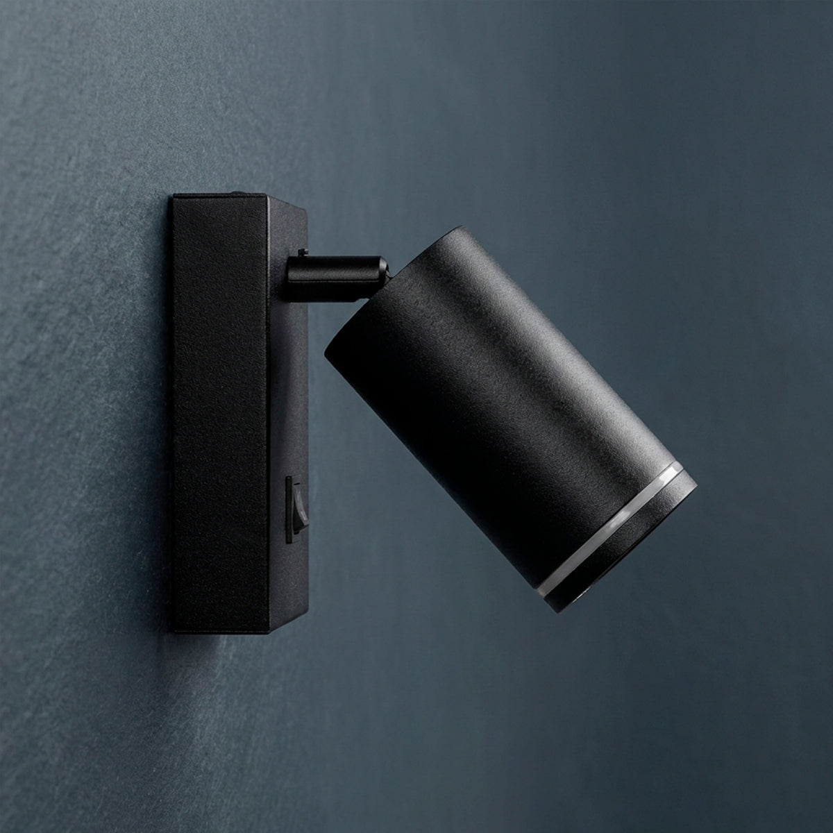 Luminaria de acento para pared en acabado negro mate con cabezal cilíndrico orientable.
