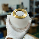 Mano con guante blanco sosteniendo una esfera de vidrio opalizado blanco para la luminaria Collier Gold.