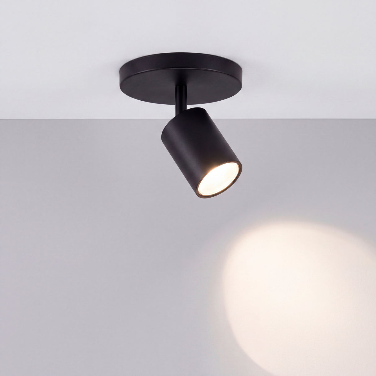 Foco técnico encendido proyectando un haz de luz suave sobre pared blanca de estilo minimalista.