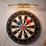 Lámpara de pared Nerina iluminando una diana de dardos, ideal para zonas de juegos.