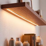 Luz lineal continua oculta debajo de un estante flotante de madera, optimizando el confort visual.