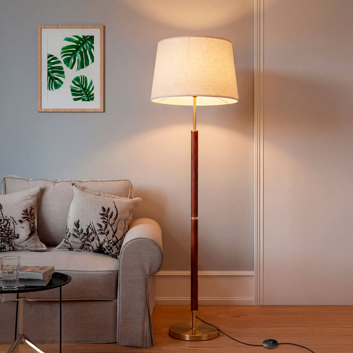 Lámpara de madera y oro encendida en una sala junto a un sofá de tonos neutros.