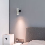Baño de luz cenital focalizada sobre mesa de noche mediante un discreto proyector tubular de pared.