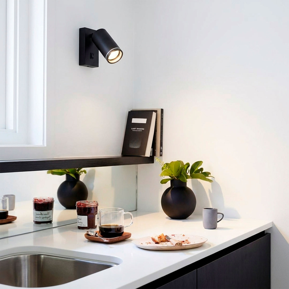 Foco de pared negro direccional iluminando zona de trabajo en cocina de diseño contemporáneo.