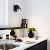 Foco de pared negro direccional iluminando zona de trabajo en cocina de diseño contemporáneo.