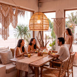 Grupo de amigos cenando bajo la luz de una luminaria artesanal en terraza costera.