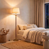 Luminaria esbelta aportando iluminación de acento cálida junto a una cama de diseño contemporáneo.