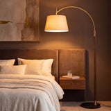 Luminaria de arco dorada junto a cama de diseño contemporáneo aportando luz cálida de acento.