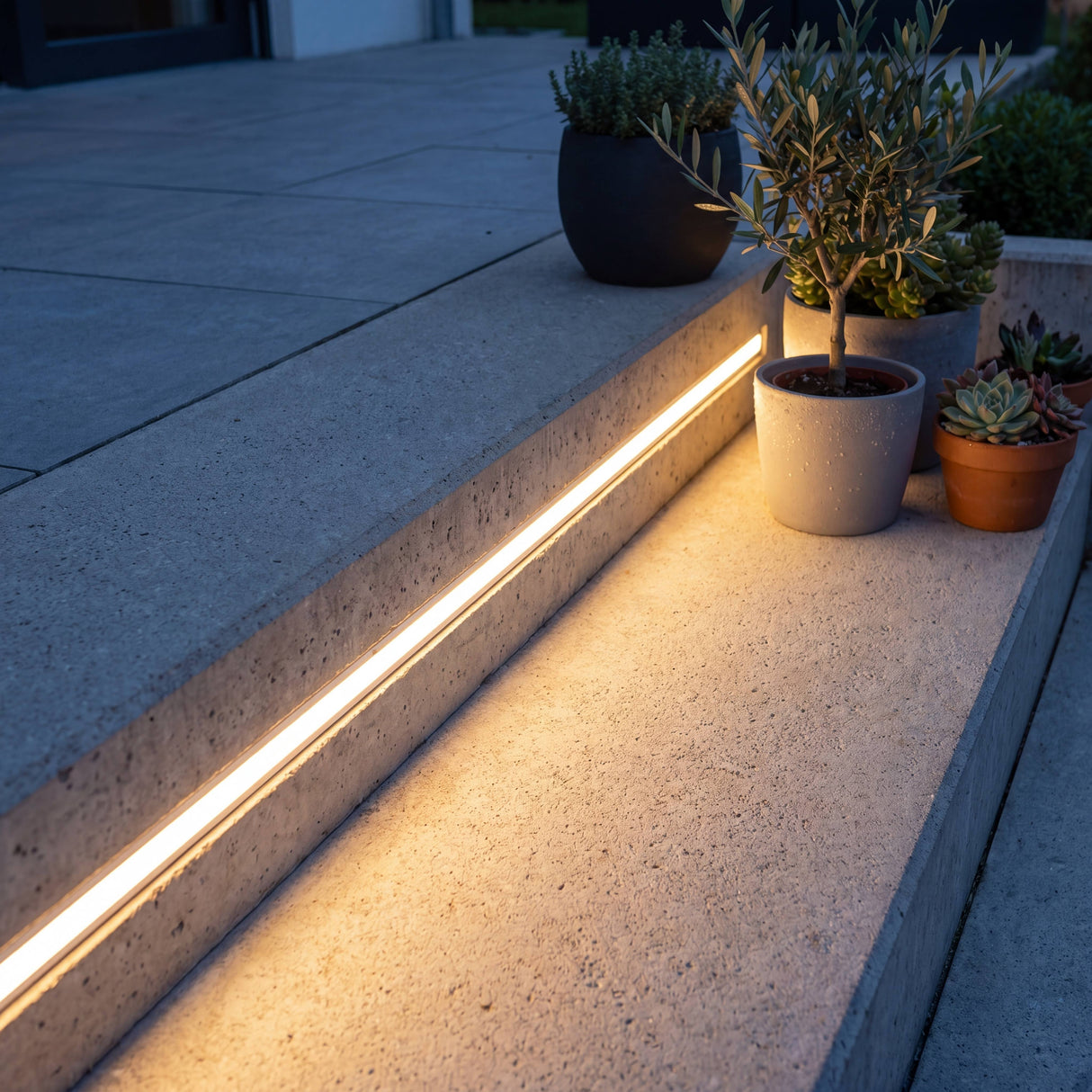 Tira LED empotrada bajo los peldaños de una escalera exterior de piedra para iluminación de cortesía nocturna.