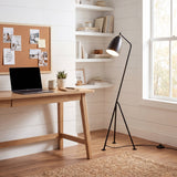 Lámpara de pie iluminando zona de trabajo con laptop y decoración funcional.