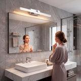 Aplique LED cromado sobre gran espejo en baño de mármol con iluminación frontal.