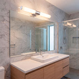 Aplique cilíndrico plata en baño revestido de mármol con iluminación neutra.
