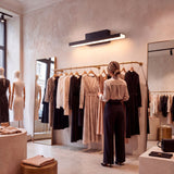Aplique negro lineal iluminando zona de percheros en tienda de ropa contemporánea.