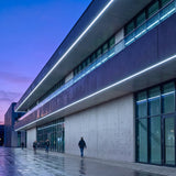 Iluminación lineal exterior acentuando la volumetría de una fachada arquitectónica moderna.