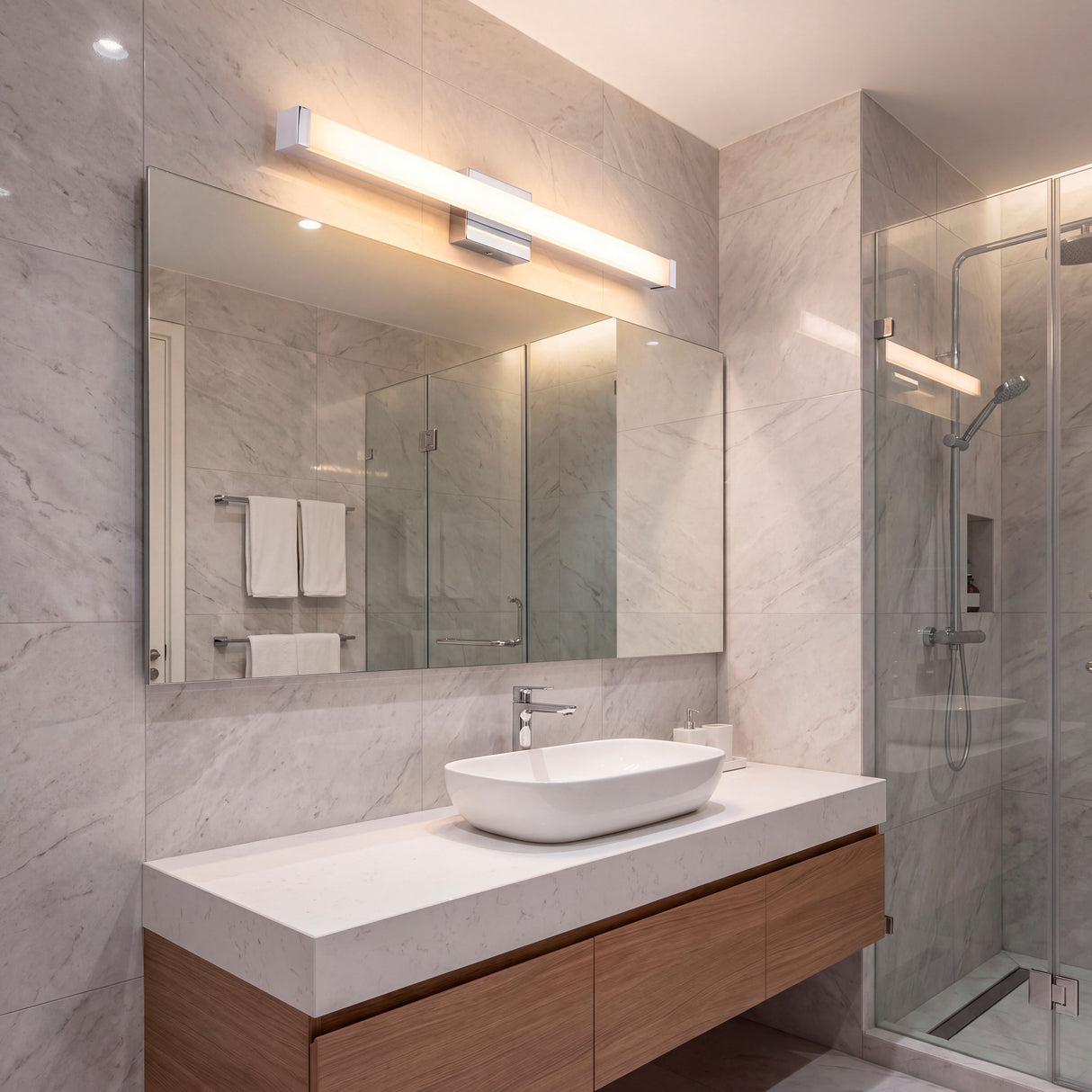 Aplique lineal Julieta instalado en baño de líneas puras con iluminación blanca técnica.
