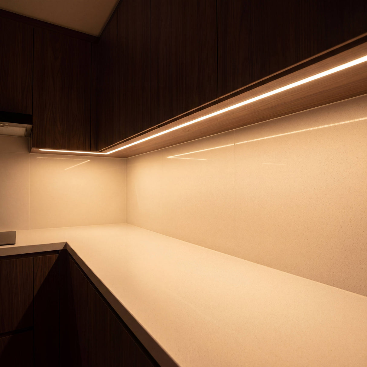 Luz cálida indirecta instalada bajo los muebles superiores de una cocina moderna para bañar la encimera.