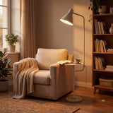 Zona de lectura minimalista con lámpara de pie blanca junto a un sillón orejero en tonos neutros.
